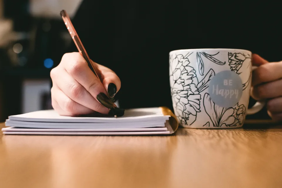 A woman writing her 5x55 method statement in a notebook next to a mug of coffee