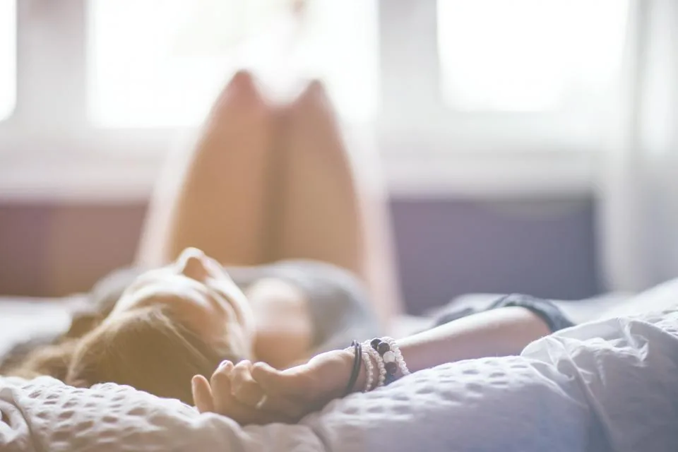 A woman lying on her bed in soft evening light, winding down with affirmations before sleep