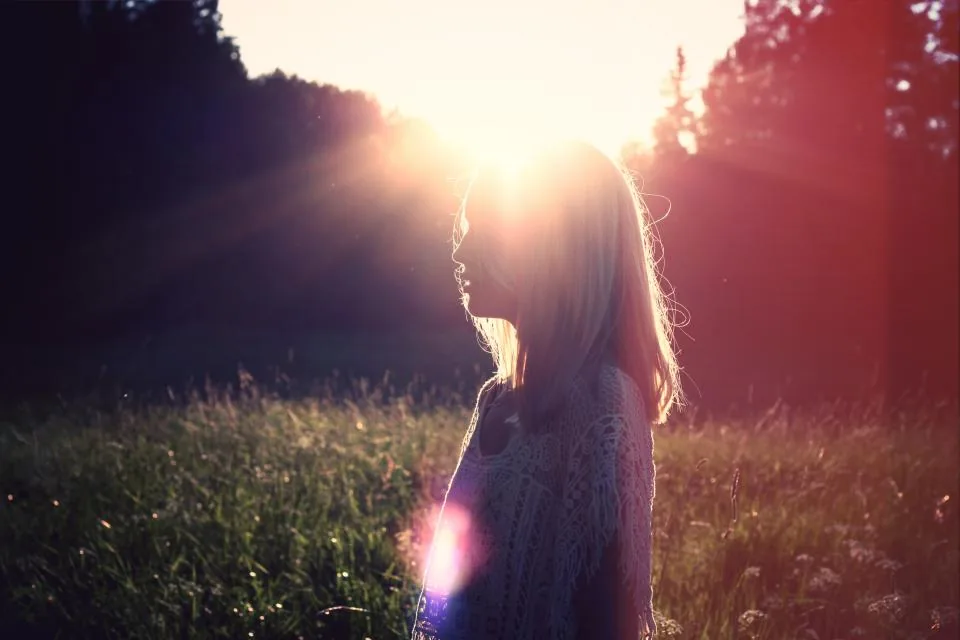A woman backlit by low sun in a meadow