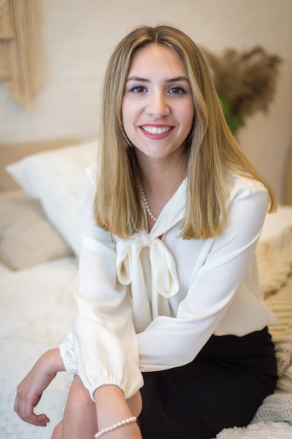 A smiling woman in a cream blouse sitting comfortably, a picture of quiet confidence