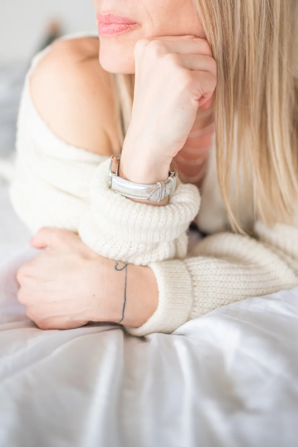 A woman in a soft cream sweater resting her head on her hand, a quiet evening moment for affirmations before sleep