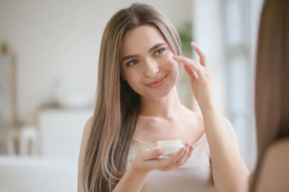 A young woman smiling at her reflection in a bright bathroom, saying a morning affirmation to the mirror
