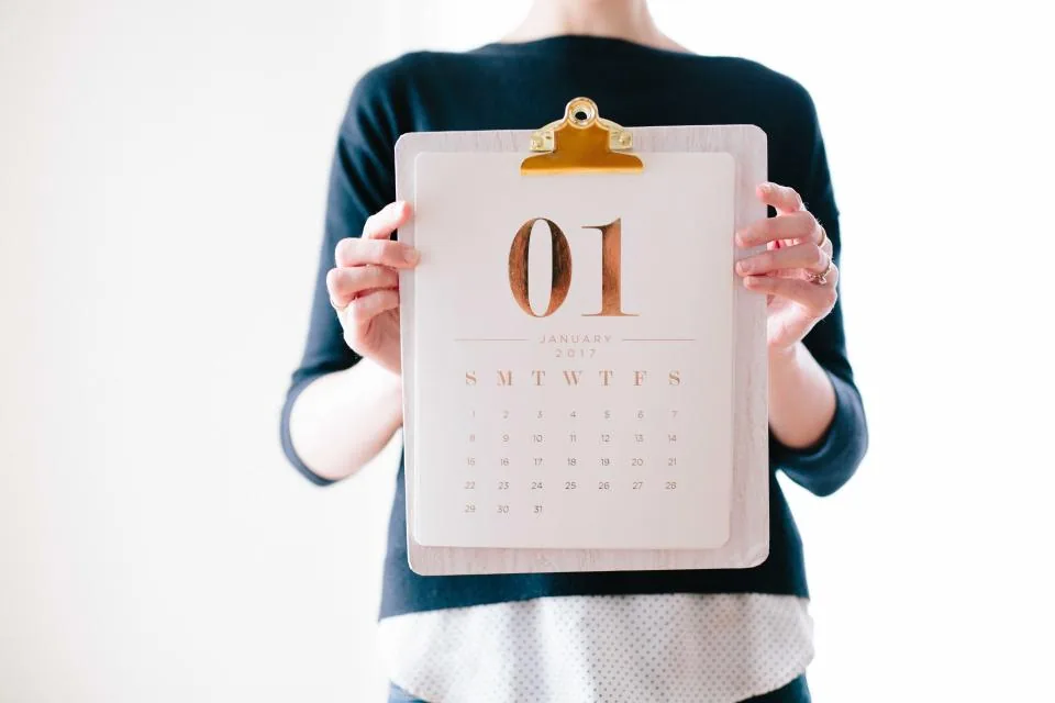 A woman holding a calendar page for the first of January, thinking about how long it takes to manifest something