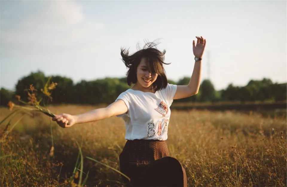 A young woman laughing and dancing through a sunny field, the carefree feeling behind lucky girl syndrome