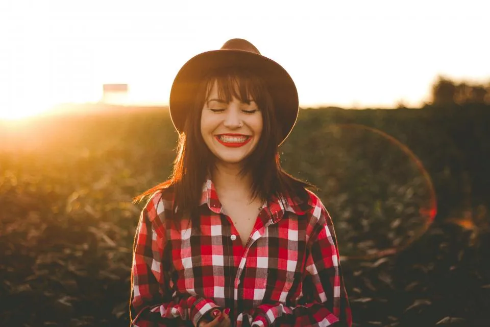 A smiling woman in a hat with her eyes closed in warm evening sunlight, feeling lucky