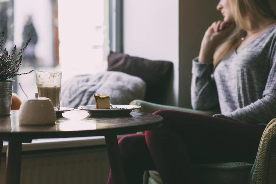 A woman sitting by a café window with a hot drink, thinking quietly