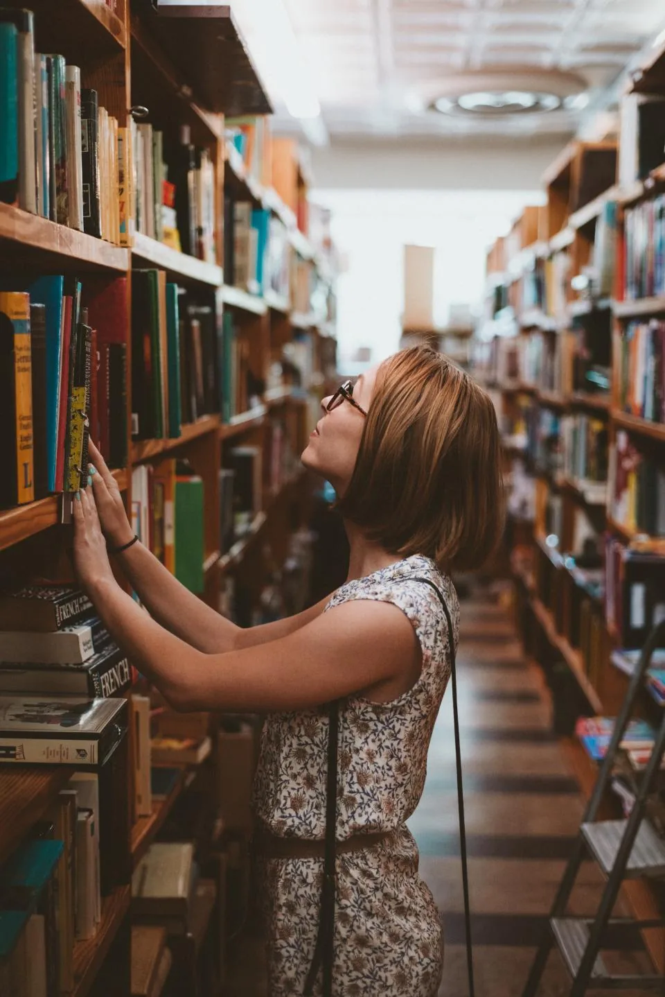 A woman in a library reaching for a book, looking up the difference between manifestation and the law of attraction