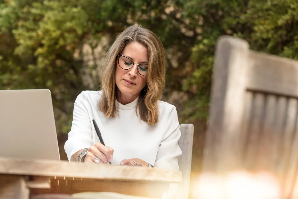 A woman writing a savings plan at a table outdoors in warm evening light