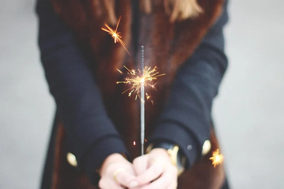 A woman holding a lit sparkler close to her chest, setting a new year manifestation intention for 2027