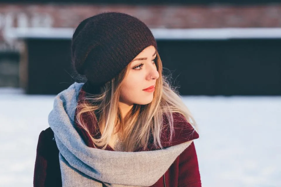 A young woman in a knitted hat and scarf looking into the winter light, thinking about her word of the year