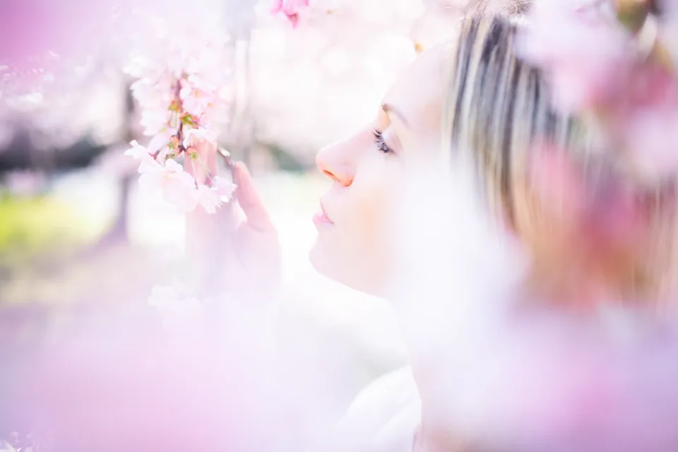A woman with her eyes half closed among pink cherry blossoms, a quiet self-love moment