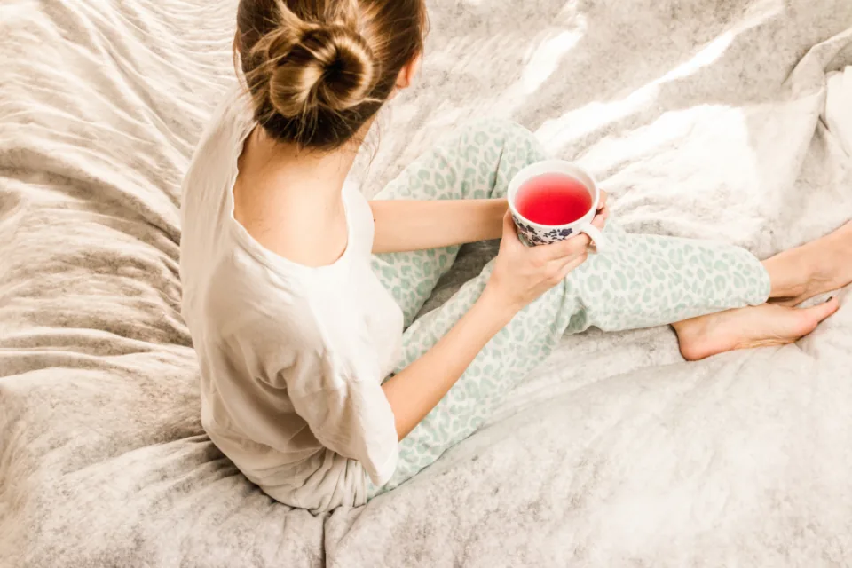 A woman sitting on her bed with a cup of tea, seen from behind