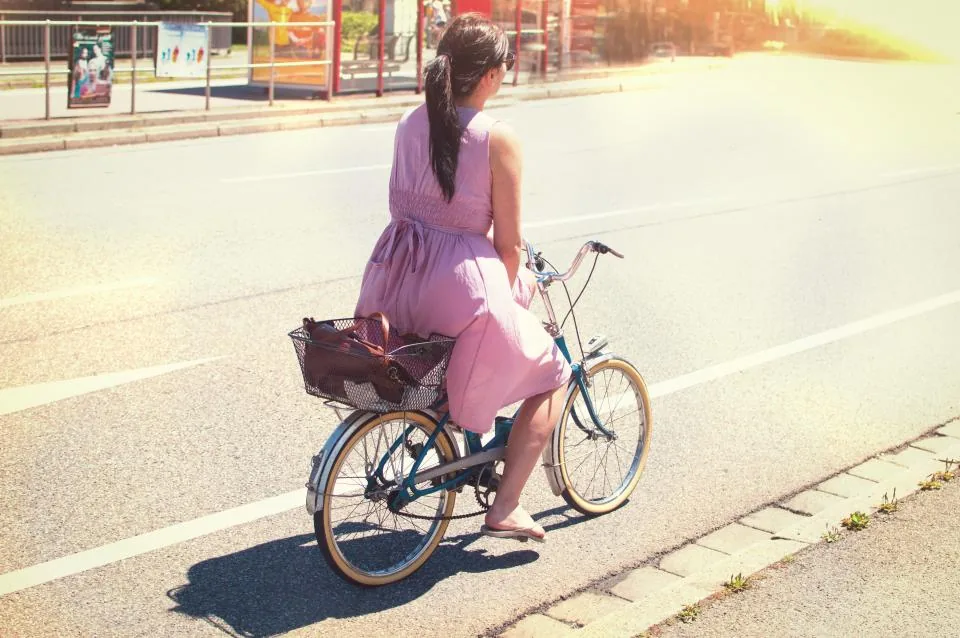 A woman in a pink summer dress cycling down a sunny street, the kind of easy day many people choose to manifest