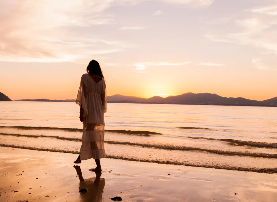 A woman in a white dress walking along the shore at sunset, a classic vision board image
