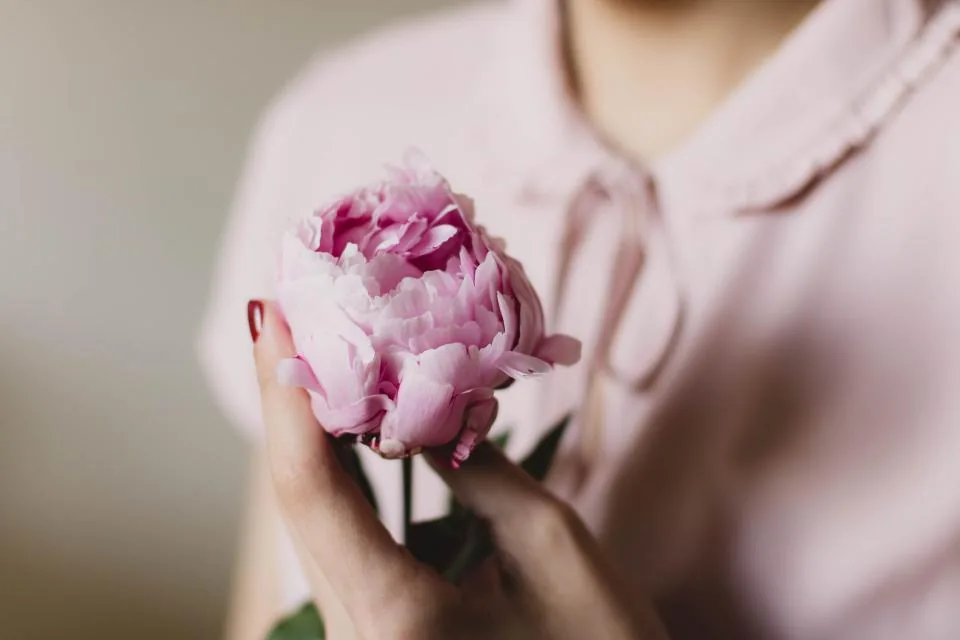 Hands holding a pink peony against a blush shirt, a soft vision board picture for self-love