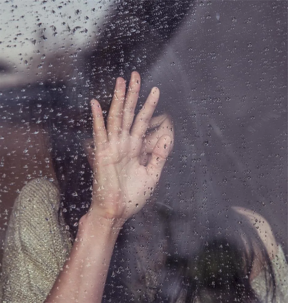 A woman with her hand pressed against a rainy window, waiting for a manifestation